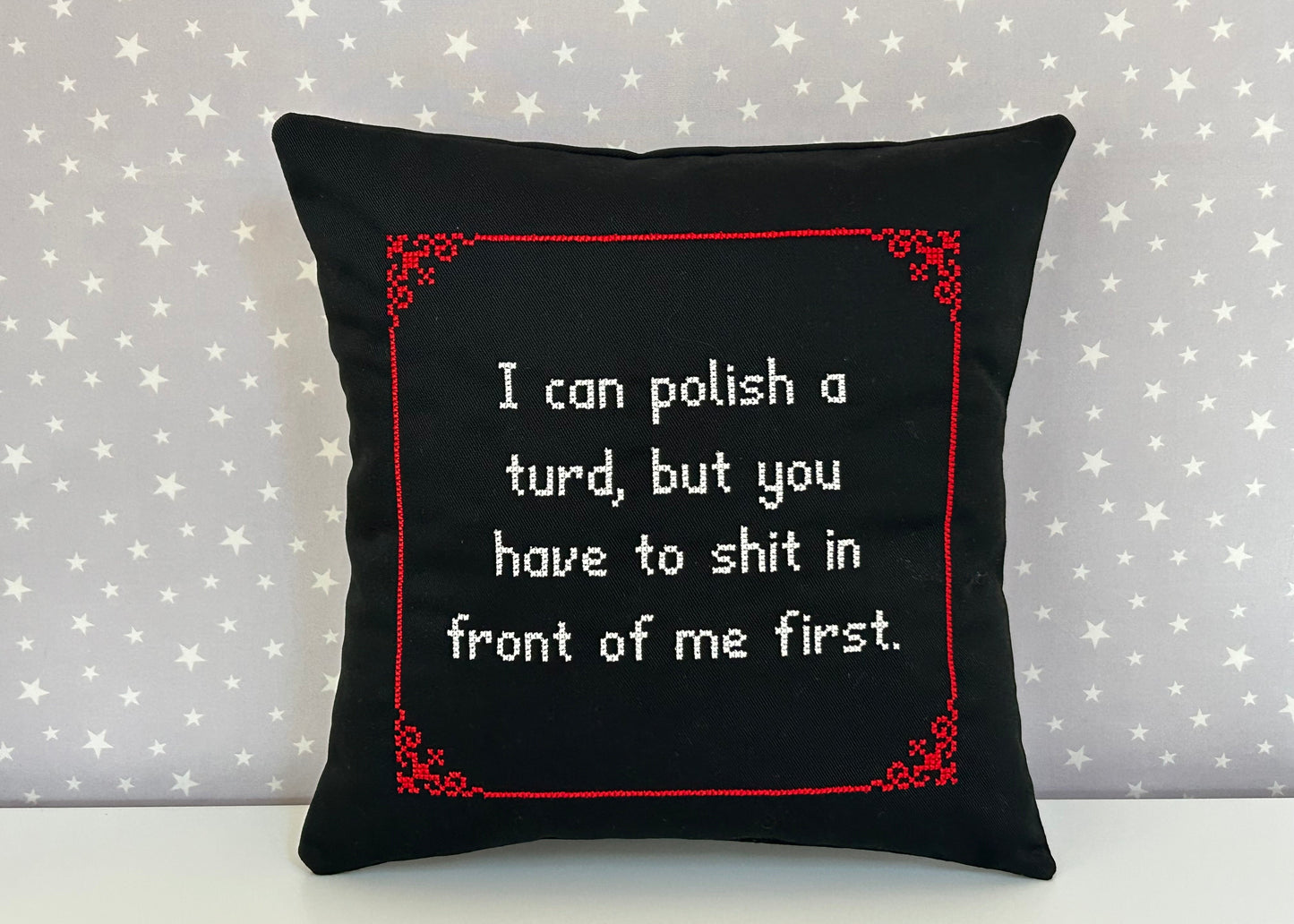 Black pillow with red border and white text on a star-patterned background
