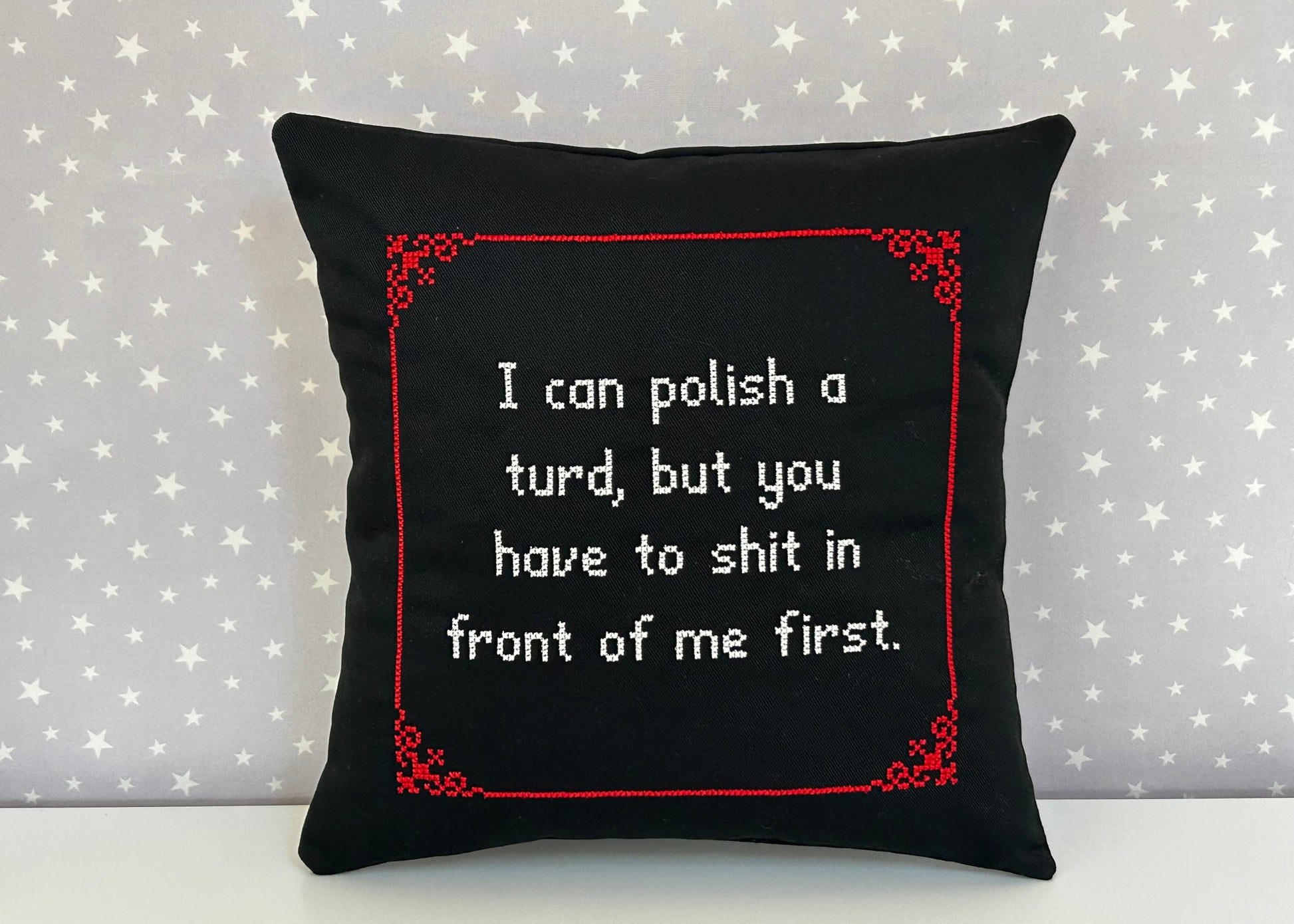 Black pillow with red border and white text on a star-patterned background