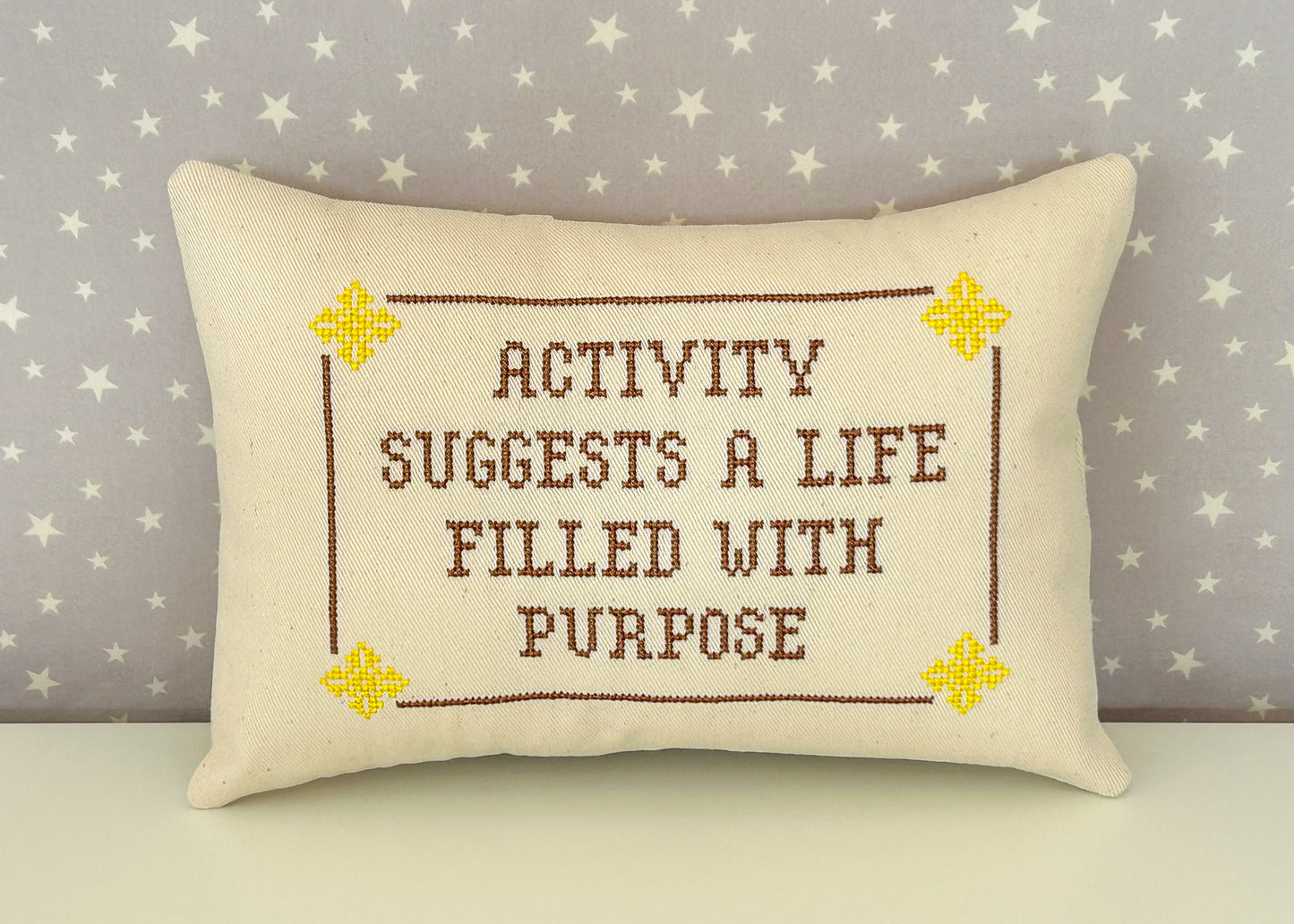 Cream pillow with yellow and brown design with the text "activity suggests a life filled with purpose"