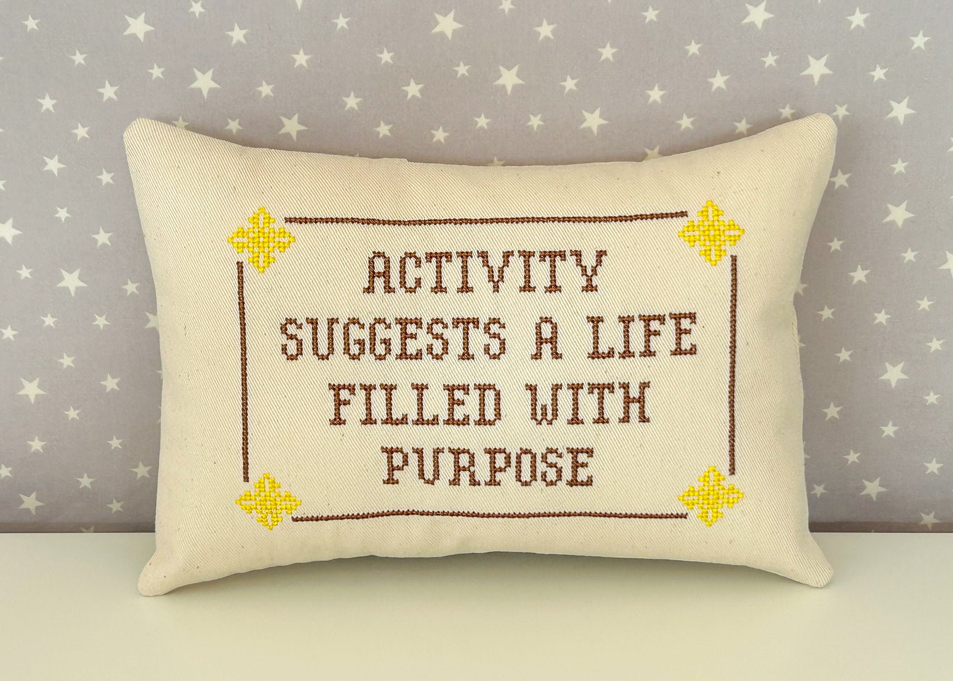 Cream pillow with yellow and brown design with the text "activity suggests a life filled with purpose"