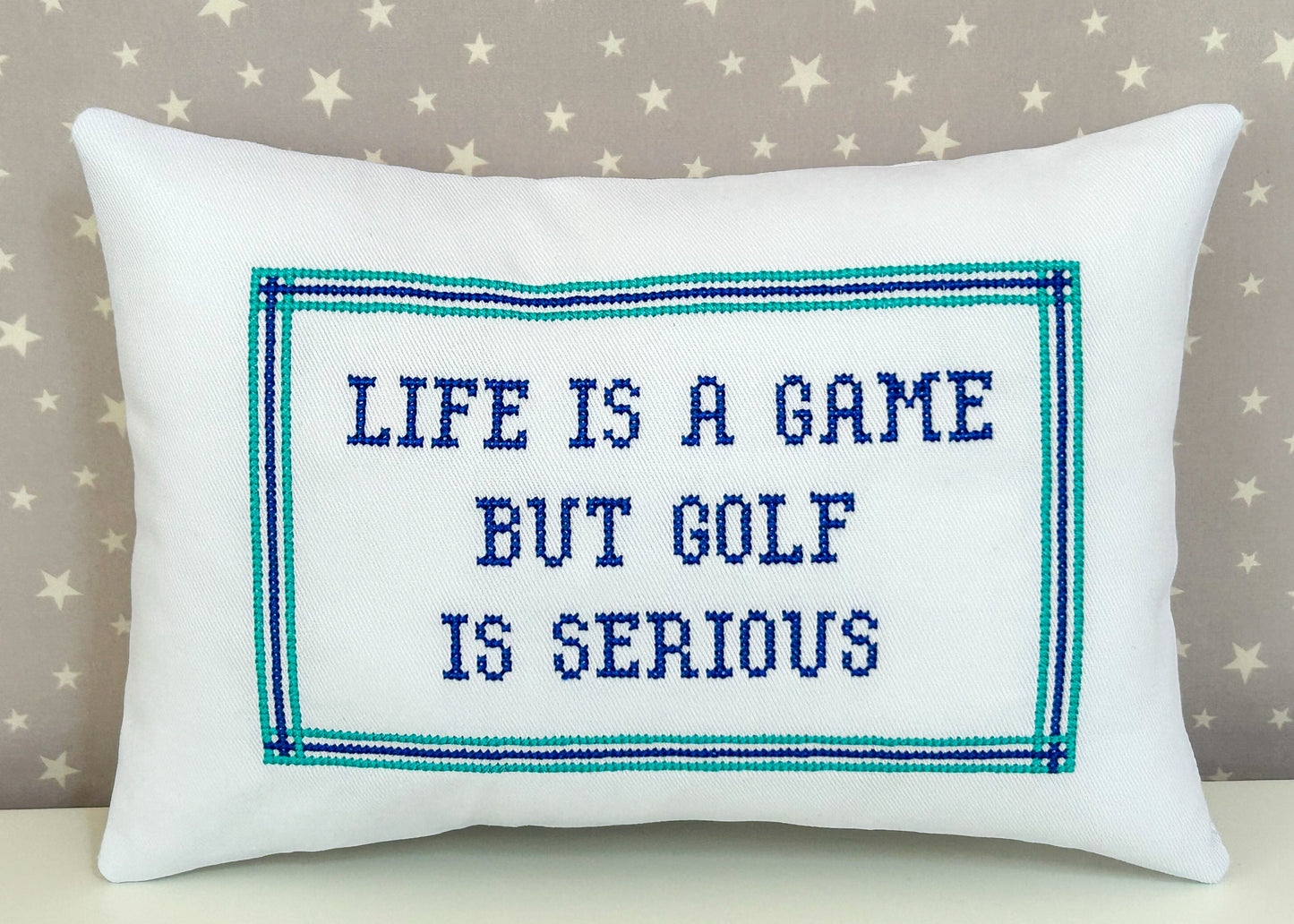 Decorative pillow with embroidered text 'Life is a game but golf is serious' on a star-patterned background.