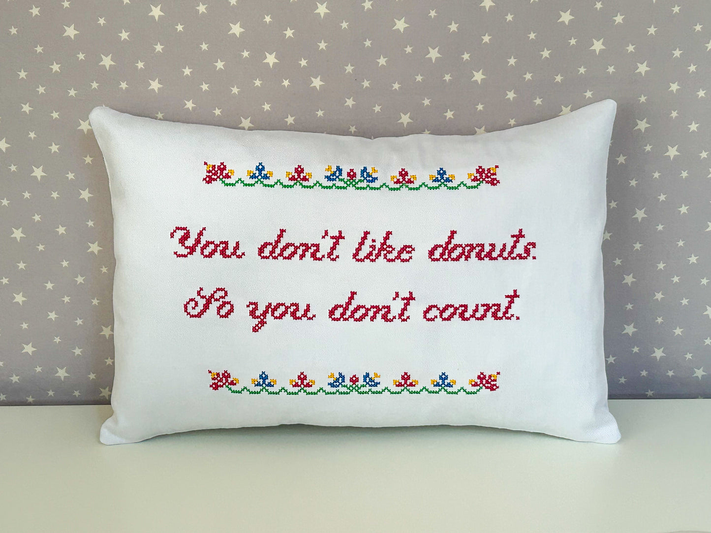 Decorative pillow with embroidered text against a star-patterned wall.
