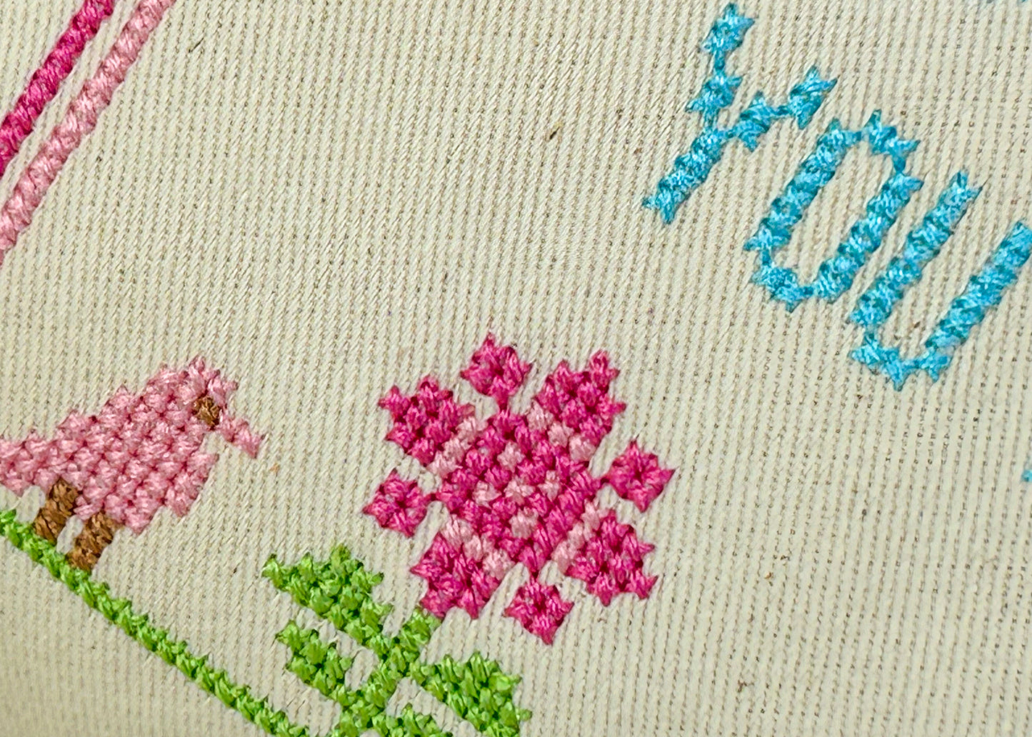 Embroidered fabric with pink flowers, green leaves, and blue text on a beige background