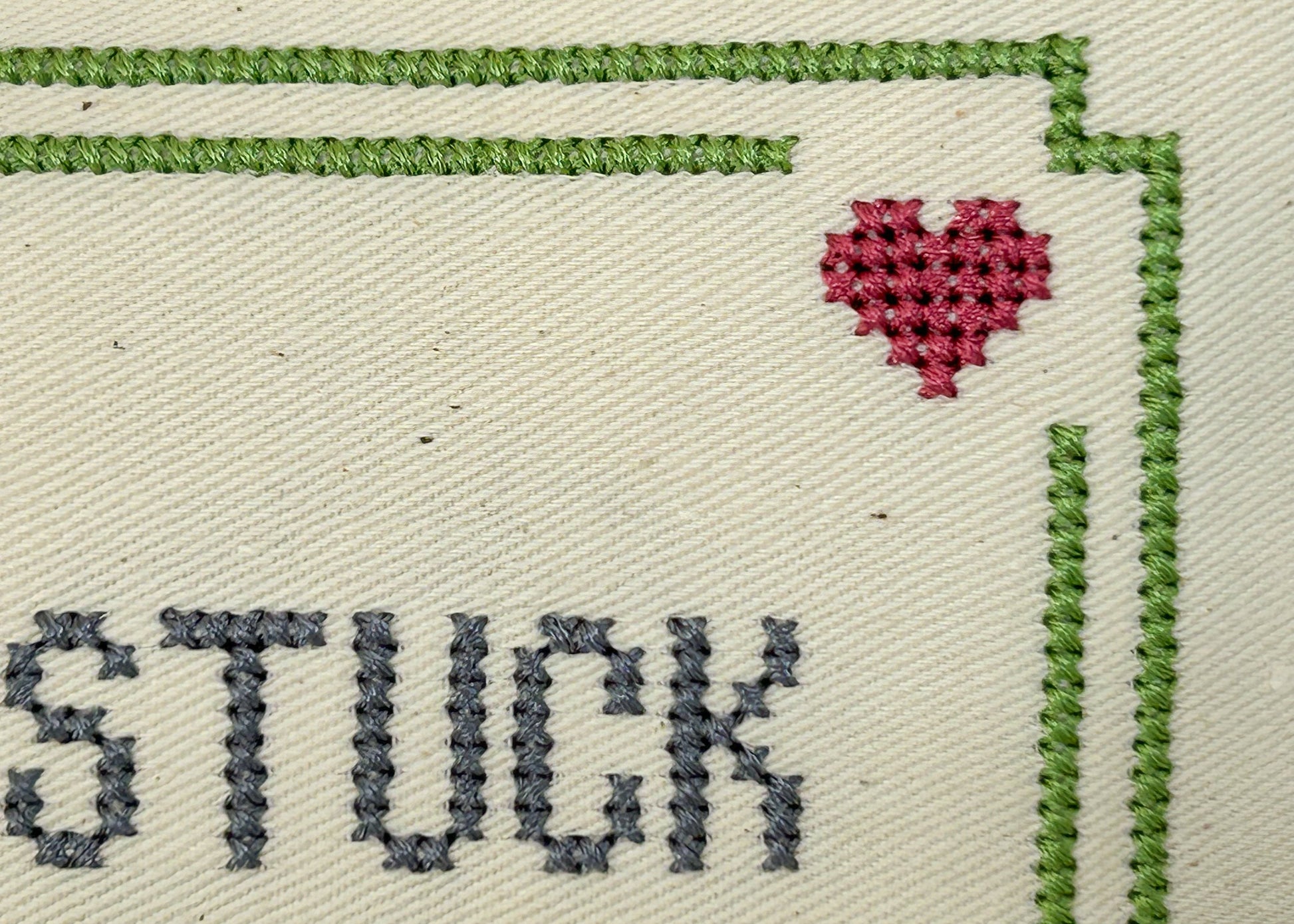Embroidery with the word 'STUCK' and a heart symbol on beige fabric.