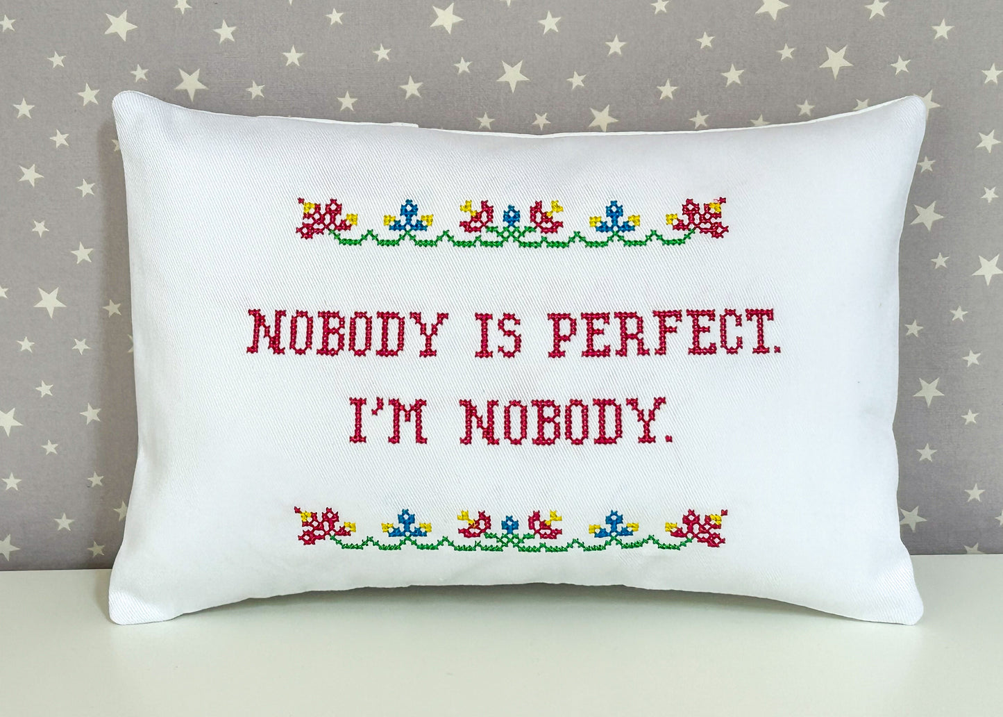 Decorative pillow with cross-stitched text and floral patterns on a star-patterned background