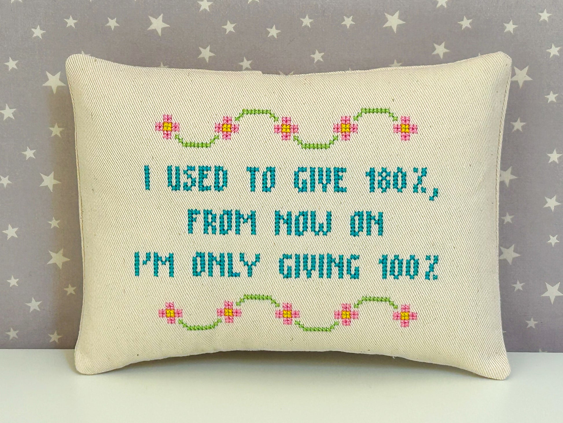 Decorative pillow with cross-stitched text and floral patterns on a star-patterned background