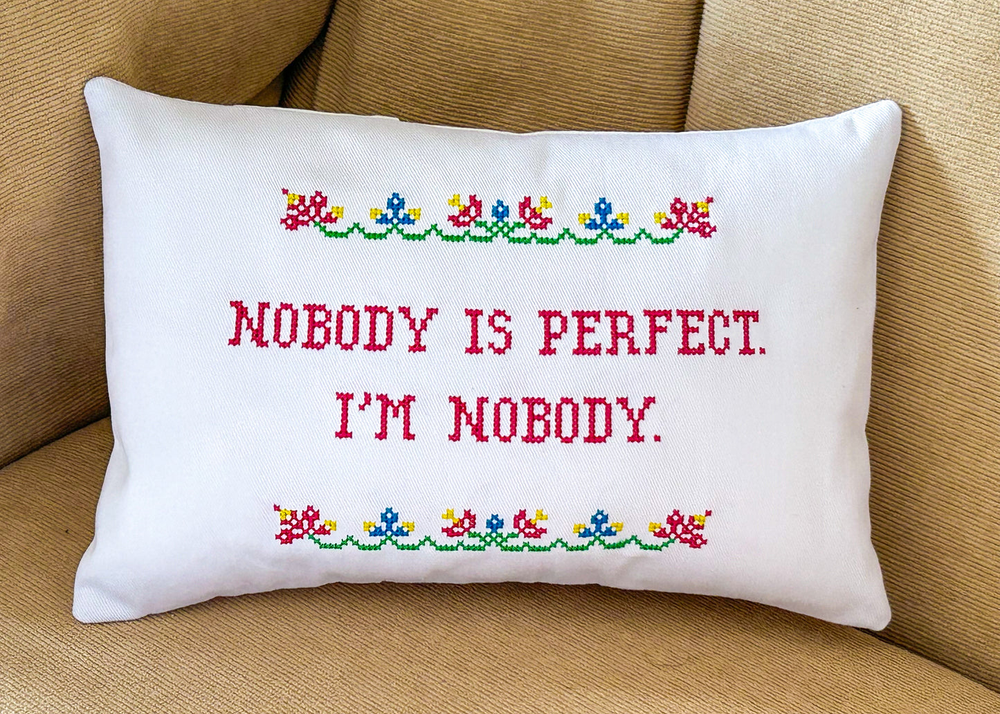 Decorative pillow with embroidered text and floral patterns on a beige couch.