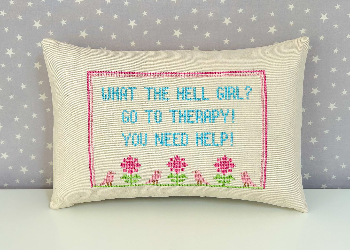 Decorative pillow with cross-stitched text and floral patterns on a star-patterned background