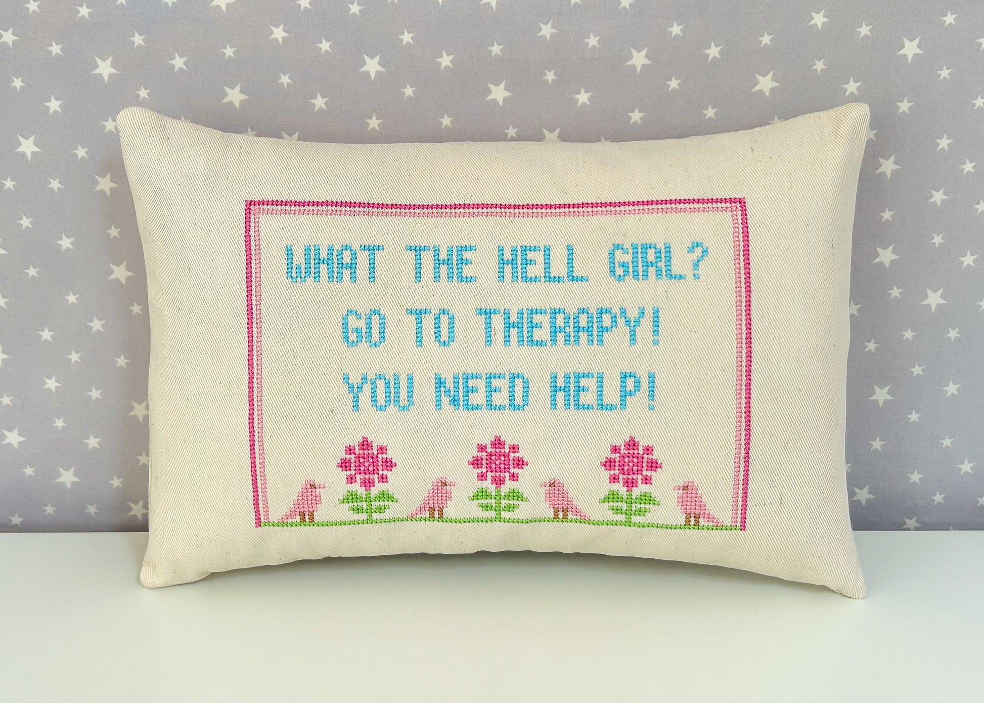 Decorative pillow with cross-stitched text and floral patterns on a star-patterned background