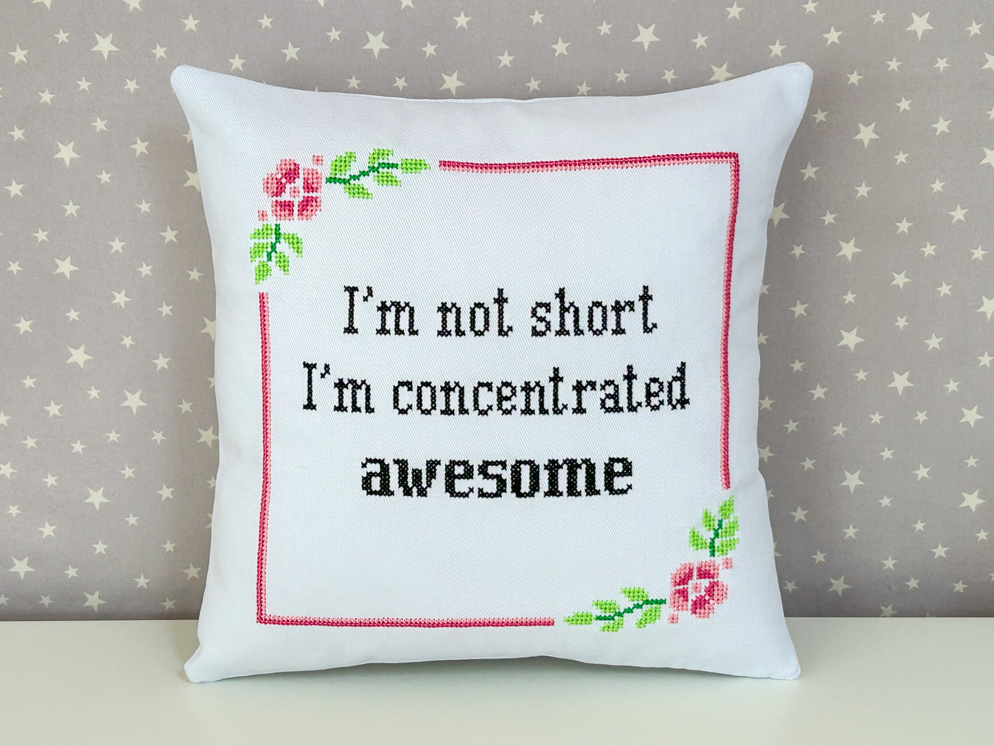 Decorative pillow with cross-stitched text and floral designs on a star-patterned background