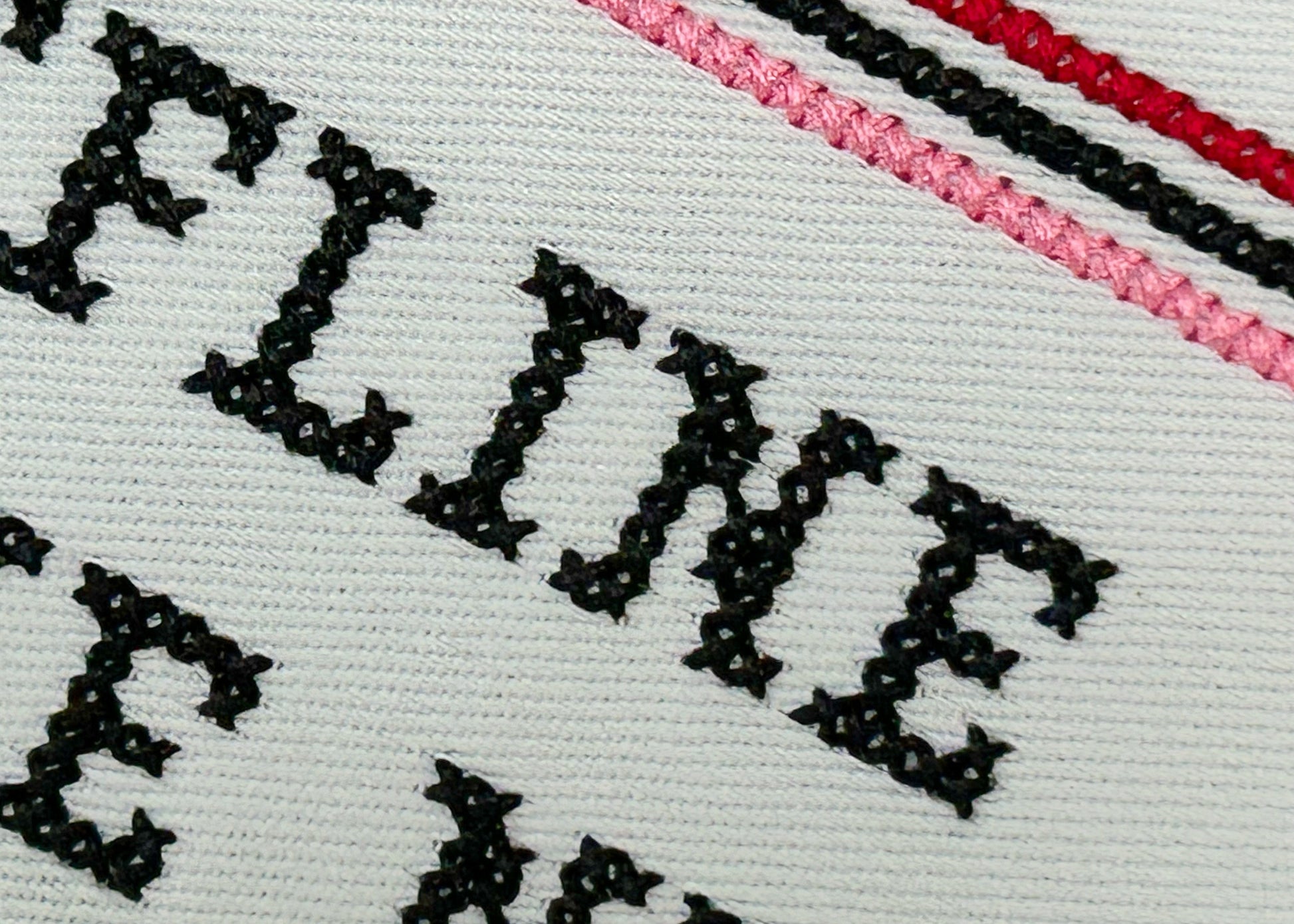 Embroidered text on fabric with black thread and a pink stripe.