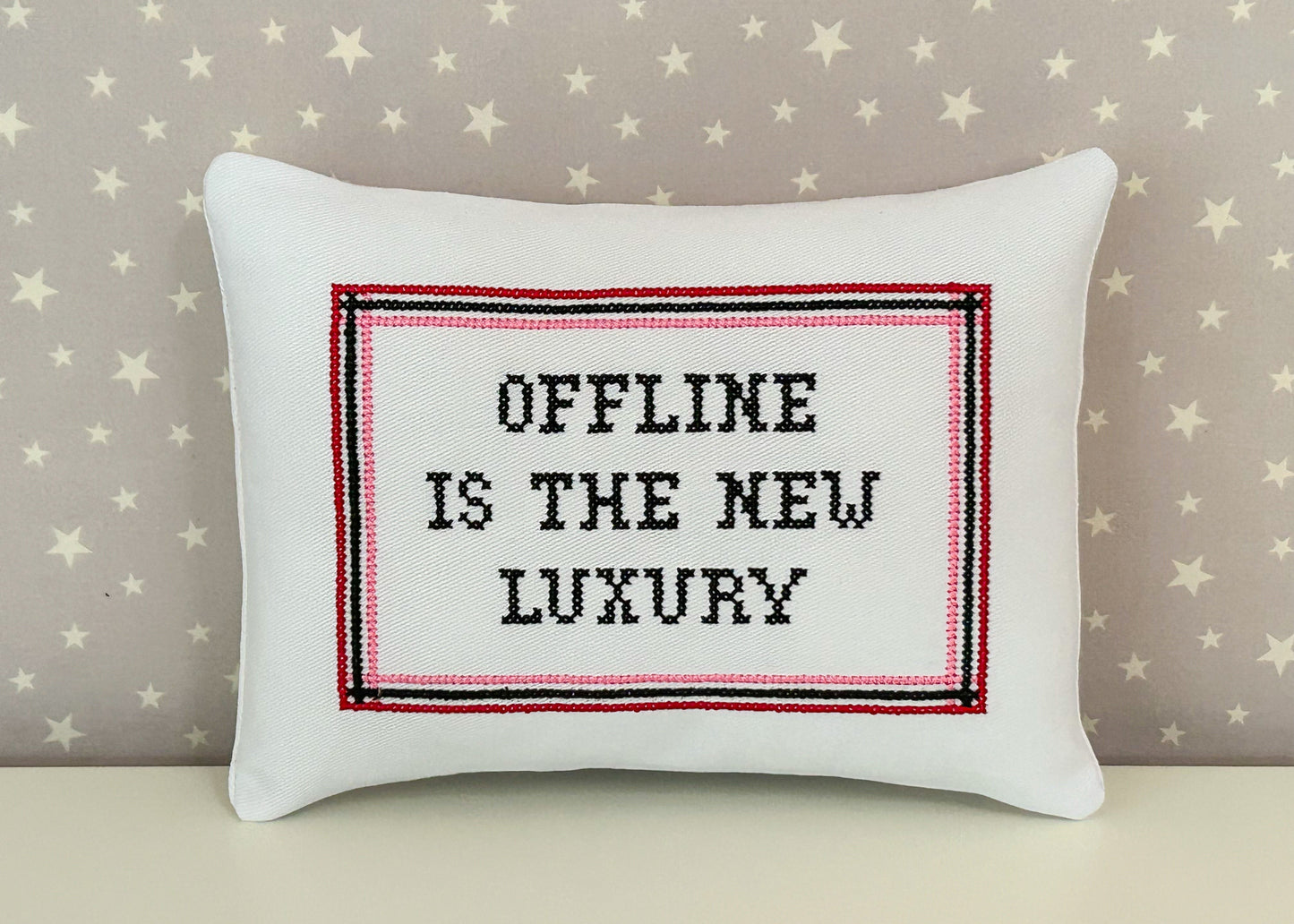 White pillow with 'Offline is the New Luxury' text on a star-patterned background