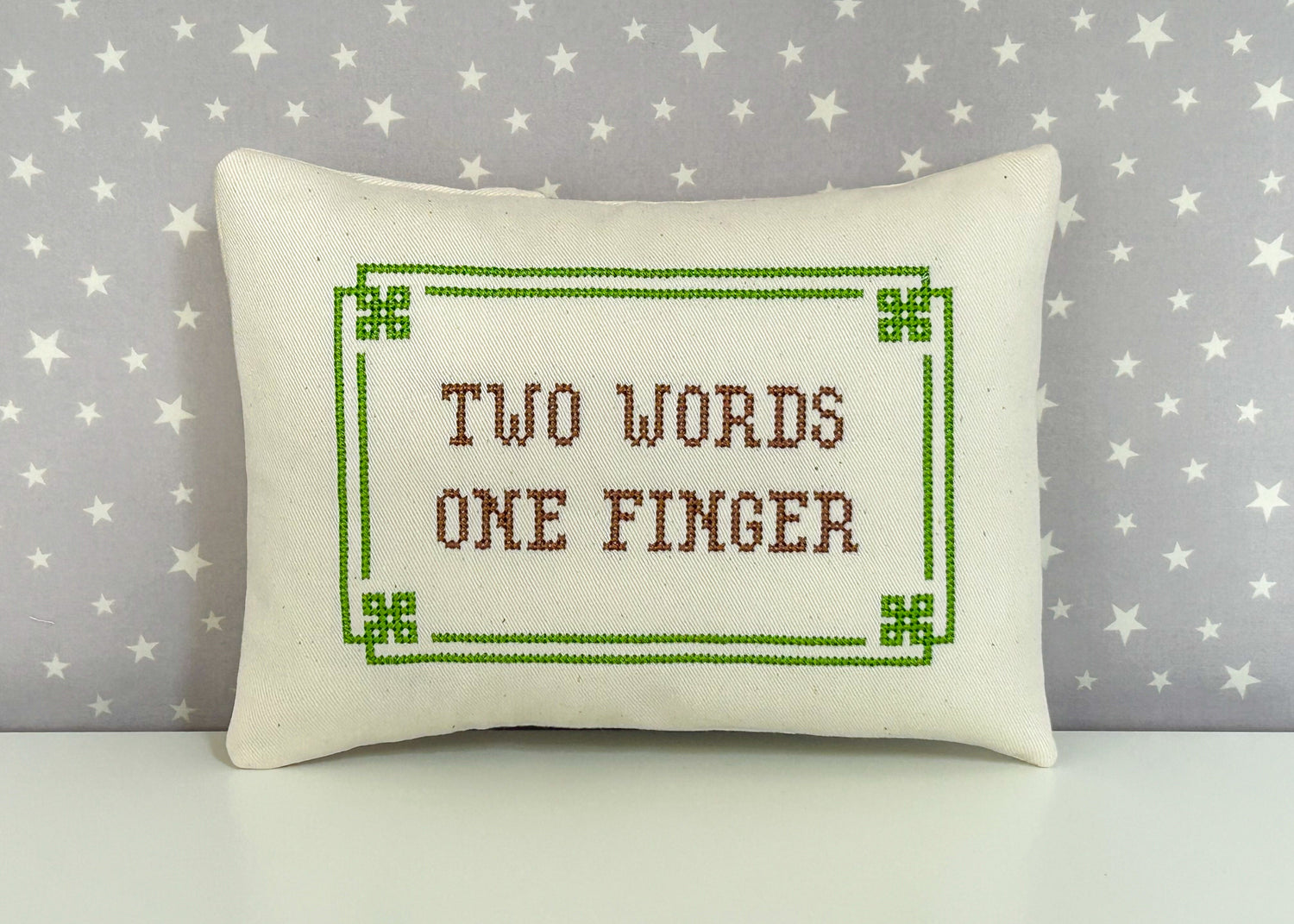 Decorative pillow with 'Two Words One Finger' text on a star-patterned background