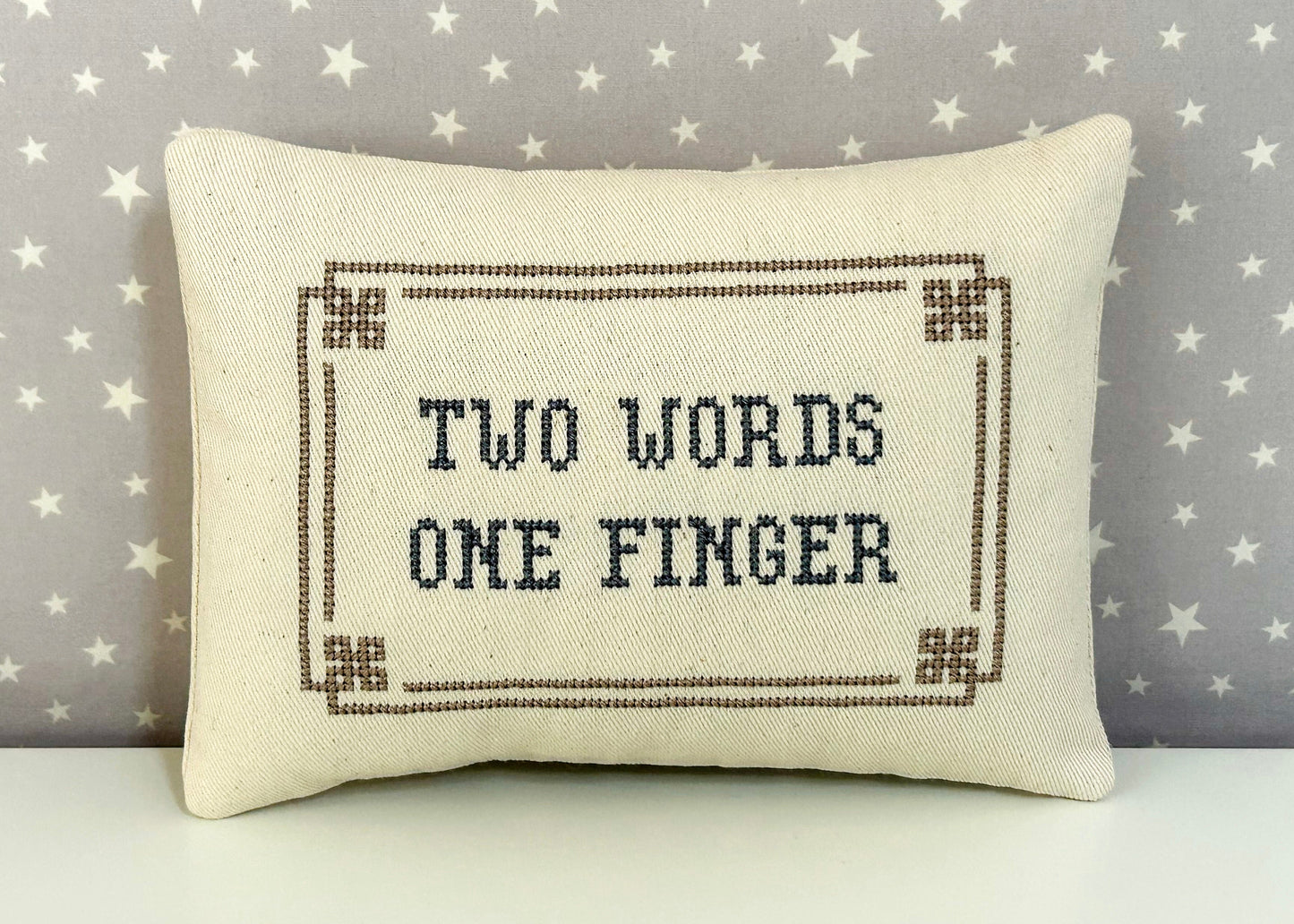 Decorative pillow with 'Two Words One Finger' text on a star-patterned background