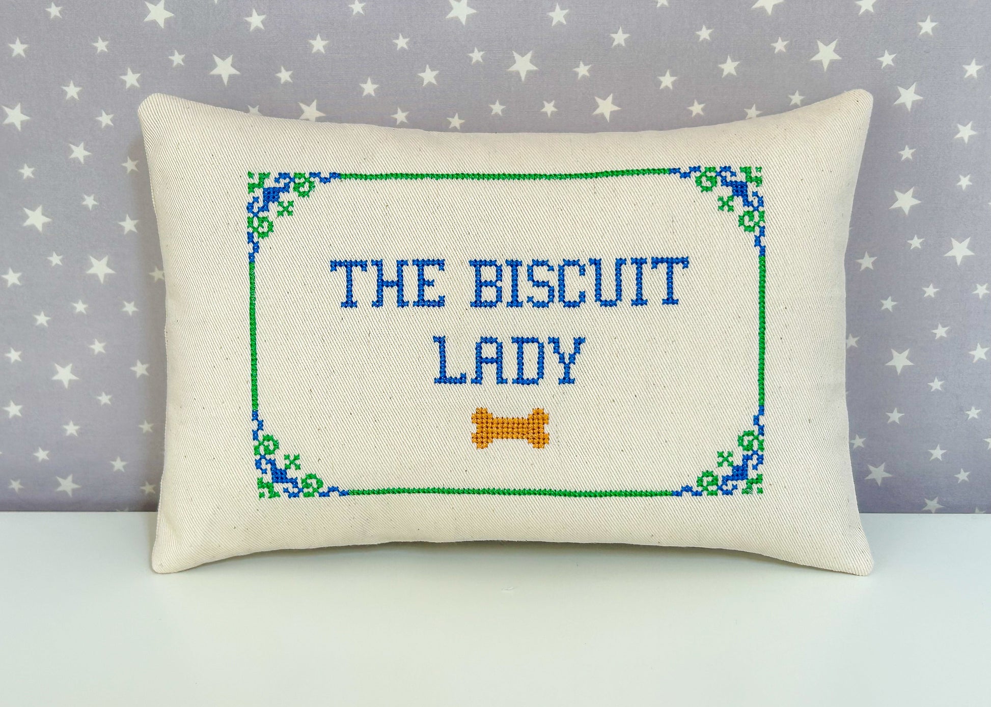 Decorative pillow with 'The Biscuit Lady' text and a bone symbol on a star-patterned background.