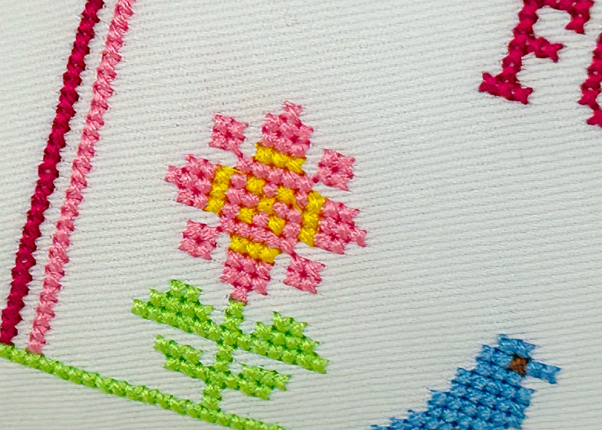 Embroidered design of a pink flower with green leaves and a blue bird on a white fabric background.